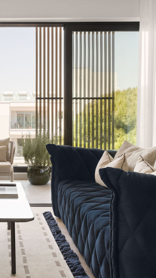 Luxury apartment view at White City Limassol Aparthotel, showing a plush navy blue sofa, floor-to-ceiling windows, and a balcony